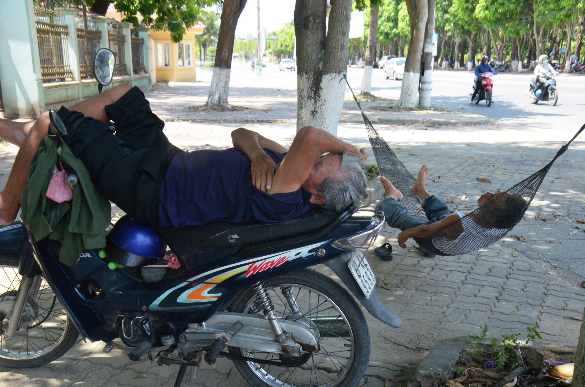 Người xe ôm và anh cửu vạn tạm nghỉ trưa dưới bóng mát ở công viên Nguyễn Tất Thành, TP Vinh, Nghệ An.