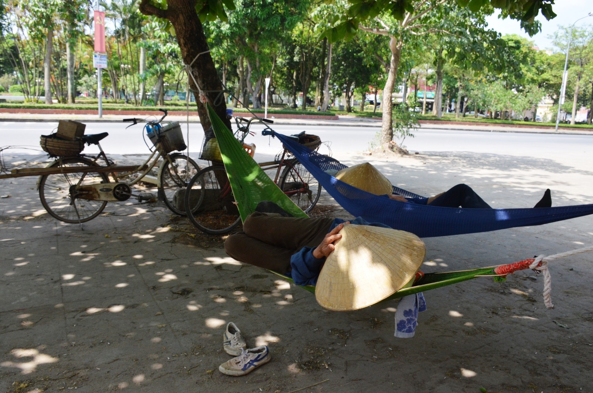 Hình ảnh hai nữ cửu vạn đang nằm nghỉ trưa tại công viên Tam giác Quỷ, phường Quang Trung, TP Vinh. Chị Nguyễn Thị Lam (42 tuổi, ở huyện Hưng Nguyên, Nghệ An) cho hay, nắng nóng ảnh hưởng đến cuộc sống của tất cả mọi người. Chính chị và những nữ cửu vạn khác cũng ít việc hơn, buổi sáng đi làm thì phải dậy sớm vì trưa nắng chẳng có ai thuê làm cả.