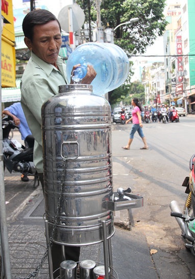 Người dân châm nước cho bình trà đá ở ngã tư Võ Văn Tần - Nguyễn Thượng Hiền.