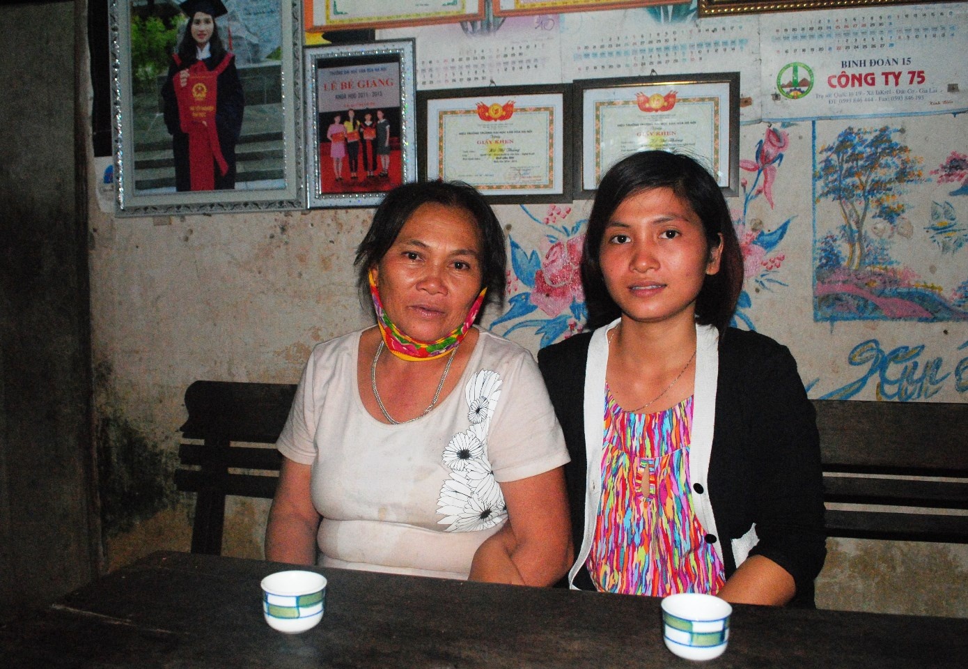 Thắng cùng mẹ trong căn nhà cấp 4 đã xuống cấp (Đằng sau là tấm ảnh chụp lúc tốt nghiệp và giấy khen sinh viên xuất sắc). Ảnh: Duy Ngợi