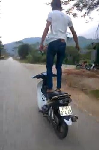 Nam thanh niên đầu trần, đứng trên yên để điều khiển xe máy. Ảnh cắt từ clip.