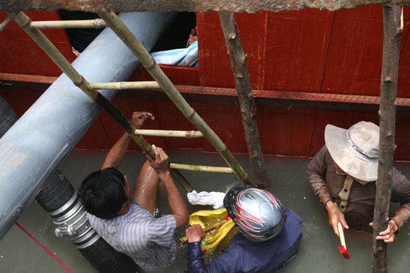 Nước dưới cống vẫn còn rất lớn, mọi người dùng ván gỗ và bao cát chèn lại. 