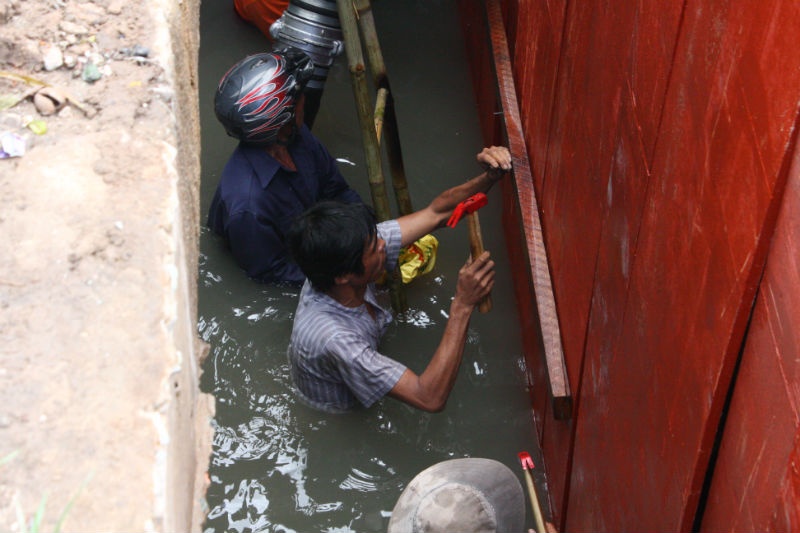 Người dân hỗ trợ lực lượng chức năng chặn cống nước để tìm kiếm đứa trẻ. 