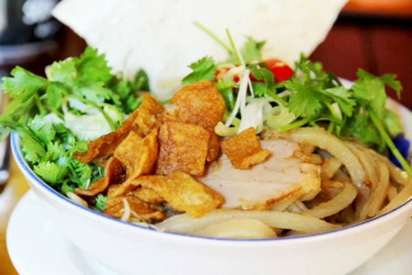 7. Cao lầu: Vẻ đẹp yên bình là một trong những điều giúp Hội An trở thành điểm đến yêu thích của nhiều du khách. Thế nhưng, không chỉ để tìm kiếm những phong cảnh đẹp cùng kinh nghiệm văn hóa phong phú, du khách đến Hội An còn bị quyến rũ bởi hương vị ẩm thực đặc sắc, trong đó có cao lầu. Cao lầu là món ăn gắn liền với hình ảnh phố cổ. Món ăn là sự kết hợp của sợi mì vàng, tôm, thịt heo, các loại rau sống địa phương nổi tiếng, giá trụng, da heo, tóp mỡ chiên giòn và rất ít nước dùng. Khi ăn cao lầu bạn sẽ thích thú khi được trải nghiệm cảm giác sựt sựt của sợi mì, đủ hương vị chua, cay, mặn, ngọt của nước mắm, rau sống, rau thơm, nước tương và tép mỡ tan trong miệng.