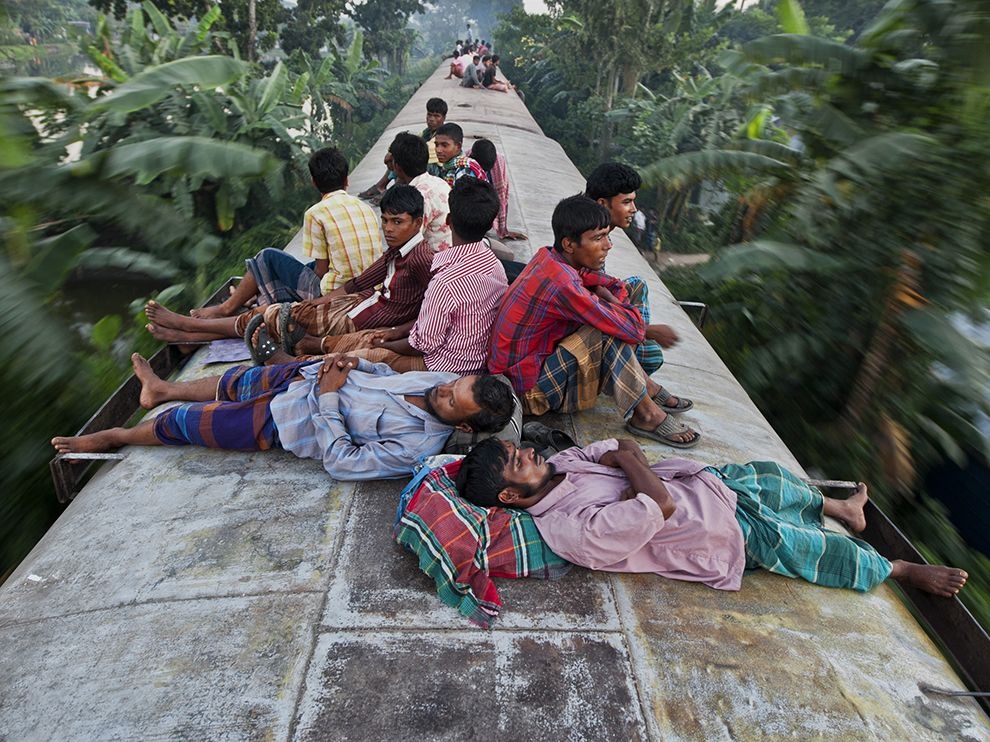 Dhaka, Bangladesh: Một con tàu lao đi giữa cây cối của vùng nông thôn, với những người đàn ông trên nóc tàu. Việc này rất nguy hiểm, nhưng đã trở thành chuyện thường ở Bangladesh, vì không đủ chỗ bên trong , hoặc đơn giản vì họ không có tiền mua vé.