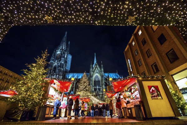 Lối vào chính của chợ Giáng sinh trước thánh đường Cologne ở Cologne, Đức, được thắp sáng và đông người qua lại.