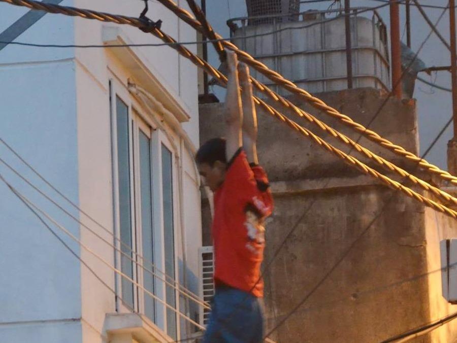 Nam thanh nien treo minh tren day dien giua pho hinh anh