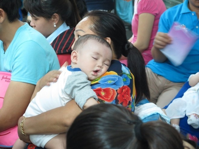 Em bé ngủ trên tay mẹ chờ đến lượt tiêm phòng. Ảnh: Khánh Trung