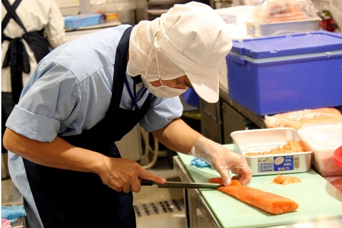 Một nhân viên cửa hàng sushi đang tỉ mỉ thái mỏng miếng cá hồi.