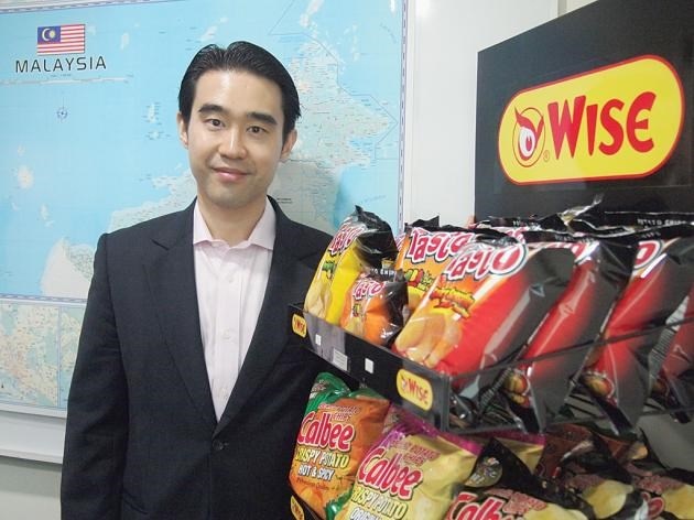 Ông Aswin Techajareonvikul chụp hình bên cạnh kệ trưng bày sản phẩm khoai tây chiên tại cửa hàng Jacy Foods (BJC), Malaysia.