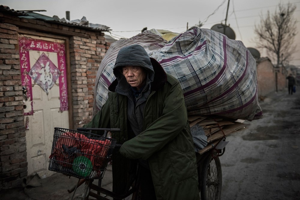 Một người đàn ông đẩy xe chứa đồ đạc thu thập được qua làng Dong Xiao Kou.