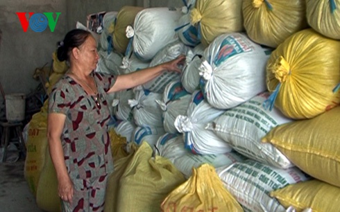 Bà Huỳnh Thị Hường bên những bao lúa lúa chất đầy nhà do thương lái bỏ cọc không mua.