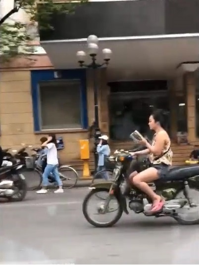 Khong mu bao hiem, co gai vua lai xe may, vua doc sach tren pho Ha Noi hinh anh