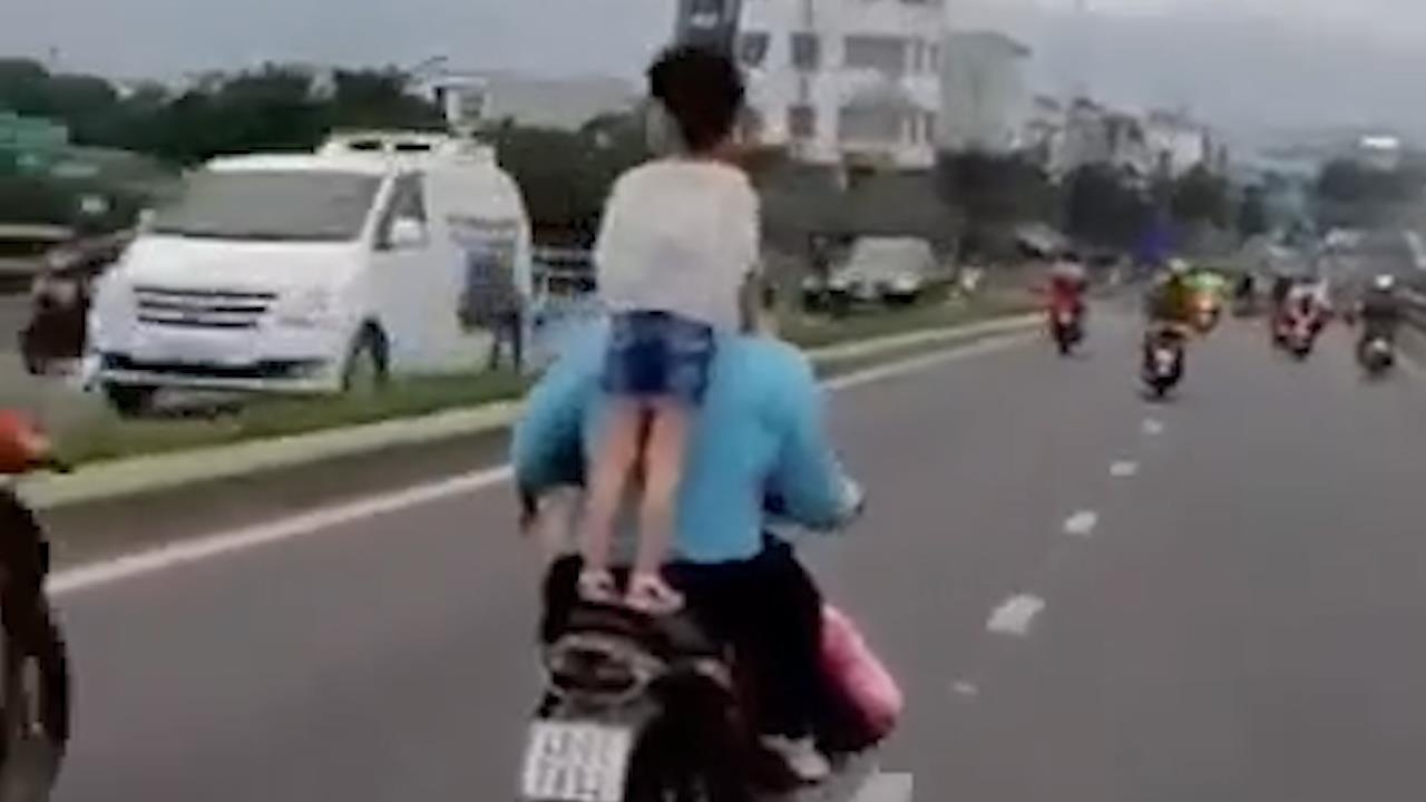 Be gai dung tren yen xe may dang lao vun vut tren duong hinh anh