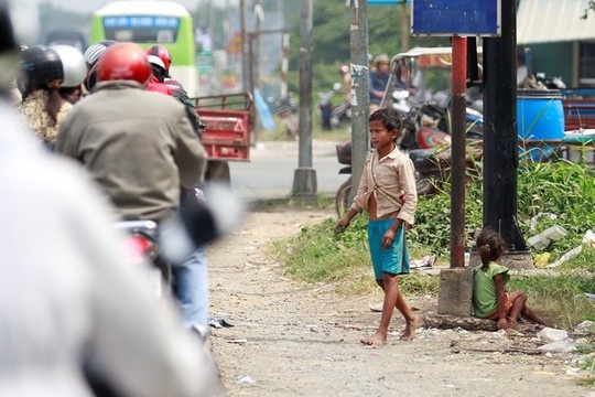 Một bé gái tầm 2-3 tuổi phải ngồi phơi nắng, trong khi một đứa trẻ khác lớn hơn tiến lại gần dòng người đang dừng xe đợi đèn đỏ