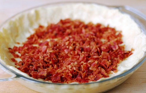 Trải tấm pastry puff lên khuôn bánh, nén chặt xuống khuôn, rắc thịt xông khói thái nhỏ lên. Rắc vụn phô-mai cheddar lên trên cùng. Đổ hỗn hợp trứng, kem lên trên.