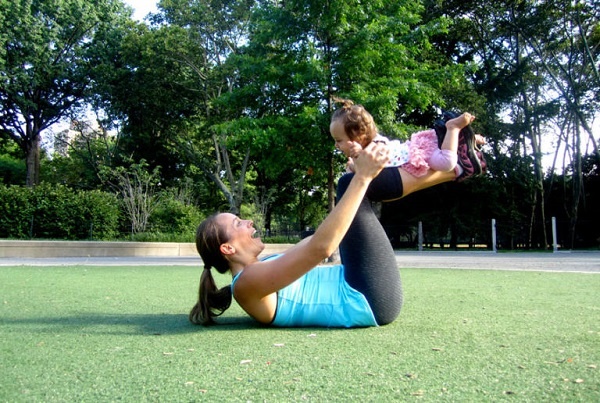 Động tác 8: Nằm ngửa, giơ 2 chân lên cao cong một góc 90 độ. Đặt bé nằm trên cẳng chân, nắm tay bé, hạ chân xuống gần chạm mông và nâng lên một lần nữa.