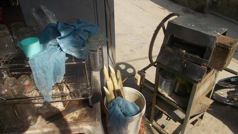Máy ép mía sau đầy những vụn bã mía. Mỗi ngày cả trăm cốc nước mía được bán ra với chiếc máy ép này.