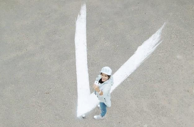 Mở đầu clip, Khả Ngân dùng bình sơn dạng xịt đánh dấu một chữ V màu trắng tại địa điểm tập trung. Cô không quên selfie bằng chiếc Samsung Galaxy V mới sắm và gửi “mật hiệu” này đến tất cả bạn bè.