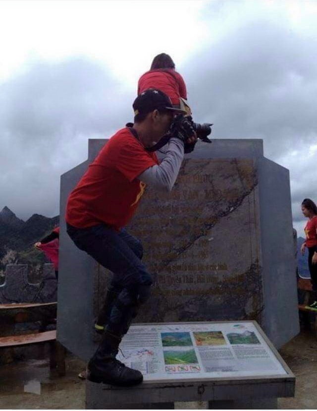 Hai bạn trẻ đứng, ngồi trên tấm bia ghi lại lịch sử con đường Hạnh phúc do các chiến sĩ thanh niên xung phong làm trên đỉnh Mã Phì Lèn (Hà Giang) - Ảnh: Facebook