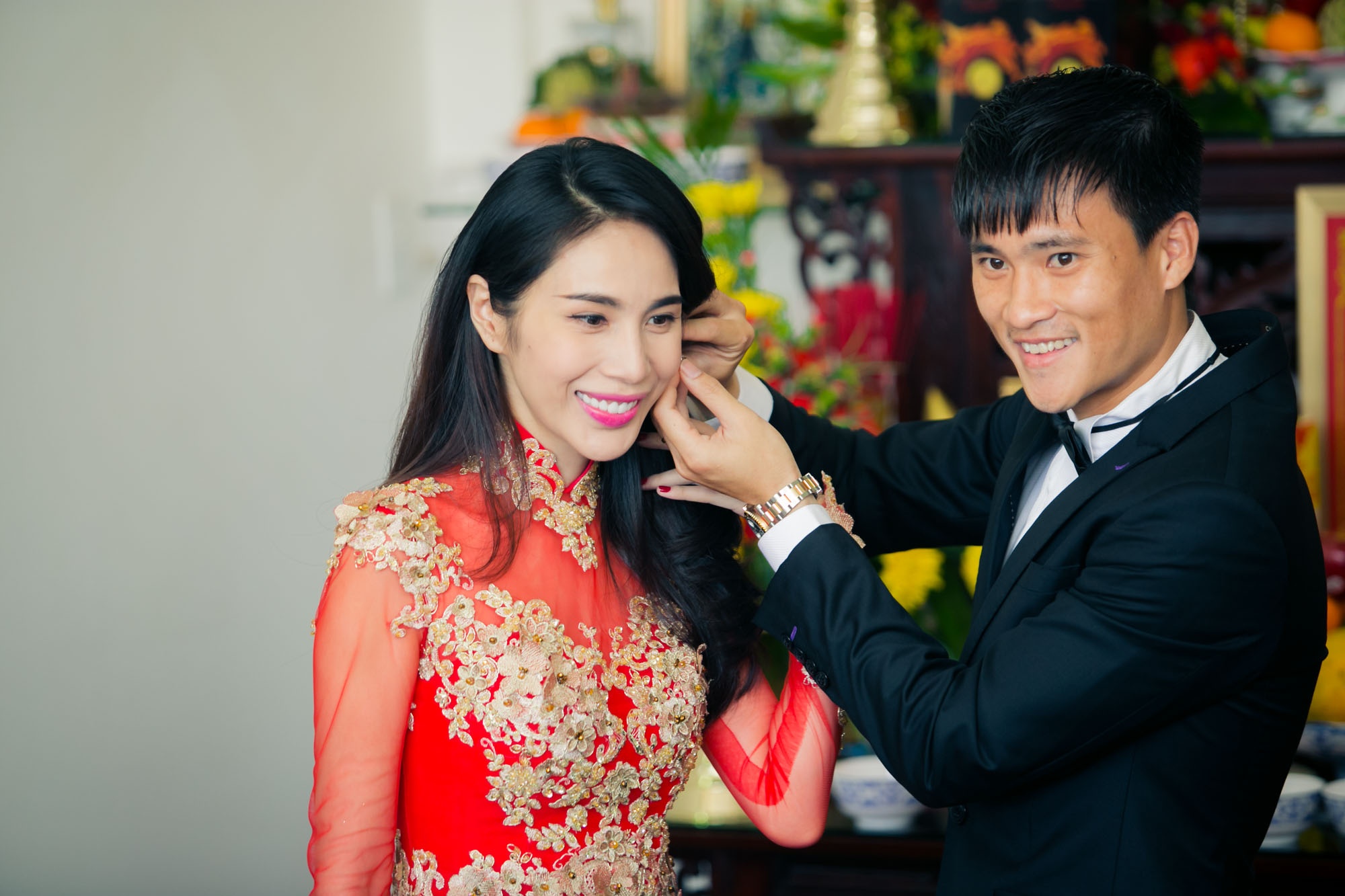 Cặp đôi rạng ngời hạnh phúc trước ống kính. Sau khi trao nhẫn, Công Vinh đeo bông tai cho vợ. Chia sẻ về chiếc áo dài, NTK Minh Châu cho biết, vì cô dâu mong muốn hôn lễ theo phong cách truyền thống, trang trọng nên họ chọn màu đỏ làm chủ đạo. Nhà thiết kế đã sử dụng vải voan đỏ để may áo dài cô dâu vì Thủy Tiên có vóc dáng đẹp, thanh mảnh. Chất liệu xuyên thấu sẽ khoe được ưu điểm của bà mẹ một con.