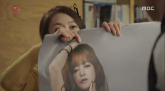 Hành động nhân vật giơ bức ảnh lộ rõ gương mặt cô gái trong tấm poster.