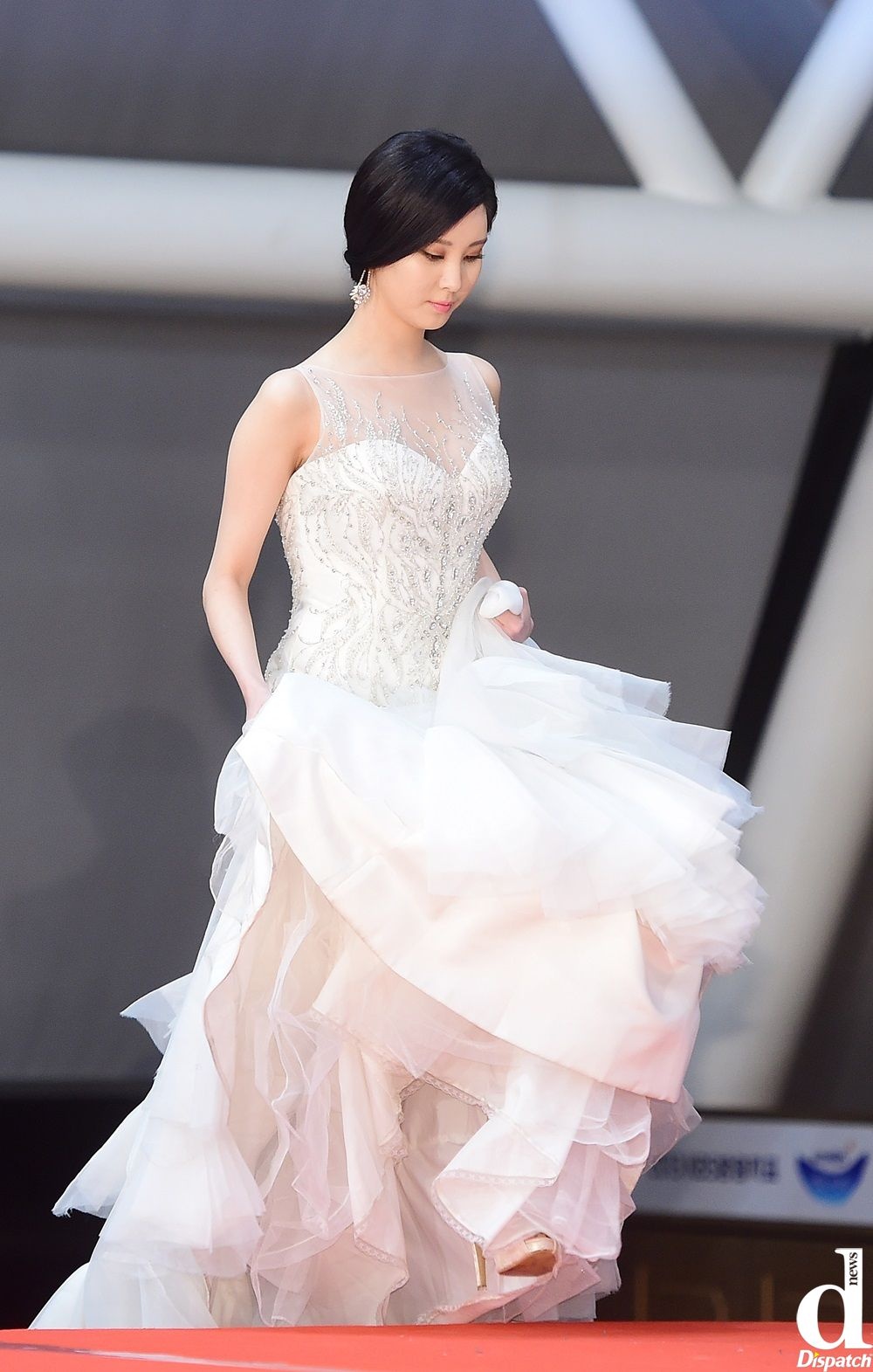 Em út nhóm SNSD Seo Hyun ra dáng cô dâu đích thực trong mẫu váy lộng lẫy. Phần thân sử dụng ren kim tuyến, thiết kế ôm sát cơ thể, chân váy xếp tầng bồng bềnh lãng mạn. Nữ ca sĩ trẻ để kiểu tóc chải rẽ ngôi đơn giản, đeo hoa tai ăn ý với trang phục.