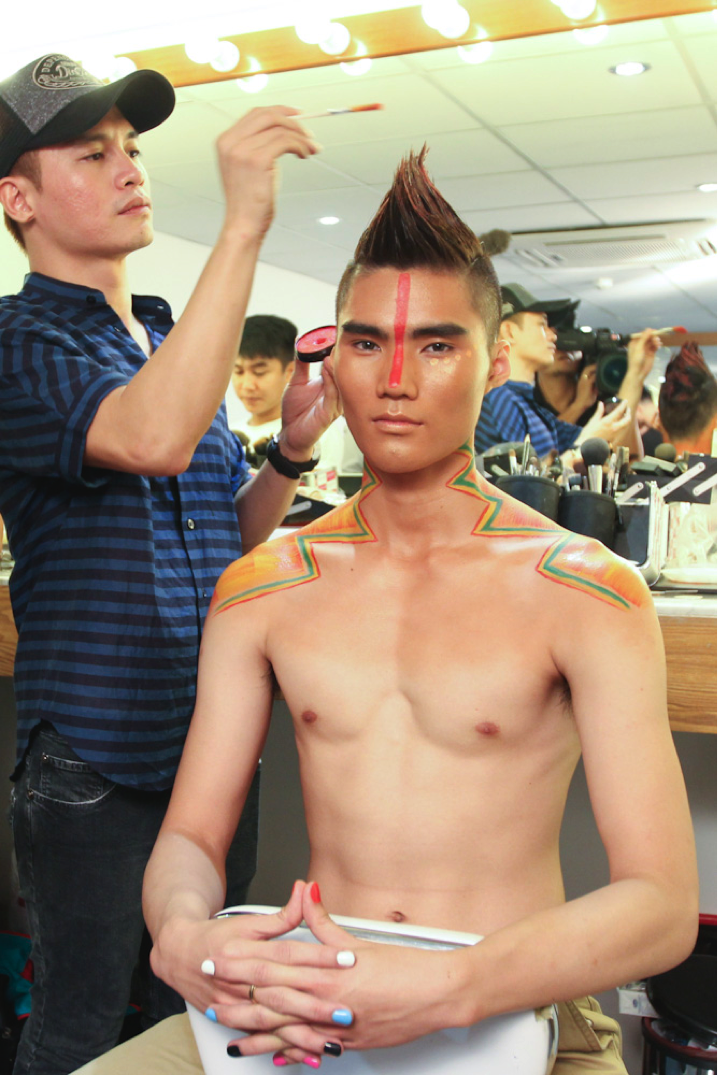 Quang Hùng được trang điểm để có làn da nâu bóng cùng những đường kẻ màu sắc và ấn tượng trên cơ thể. Sau khi mái tóc được cố định với phần chỏm dựng đứng ấn tượng, Nam Trung không quên phết thêm chút màu sắc để đảm bảo sự hài hòa trên tổng thể gương mặt cho anh.  