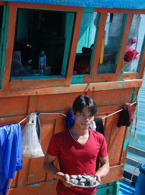 Một ngư dân lượm được đá xây dựng từ tàu Trung Quốc ném sang tàu cá.