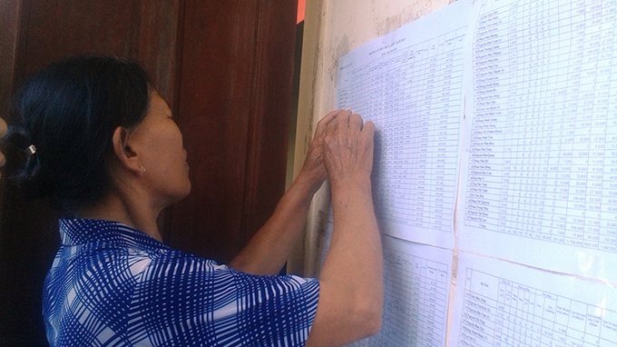 Một phụ nữ ở xóm Trà Dương, xã Quang Lộc, huyện Can Lộc (Hà Tĩnh) rà danh sách xem gia đình chị phải đóng phí bao nhiêu.
