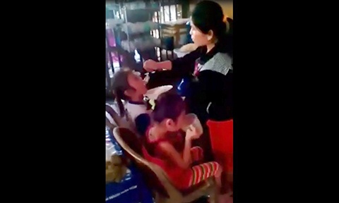 Người phụ nữ cố đút muỗng cơm đầy vào miệng bé gái.