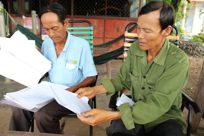 Cha của Thái Hoàng Trọng (phải) và cha của Nguyễn Hữu Nghĩa cầm quyết định bồi thường của TAND tỉnh Bình Phước đã hơn một năm nay nhưng chưa được bồi thường.