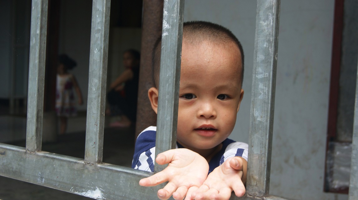 Thấy phóng viên, một cháu nhỏ chạy ra phía hàng rào chìa tay nói 