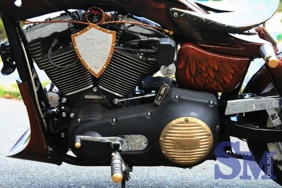 Ghi-đông được uốn hình cánh cung mềm mại mà rắn rỏi với ba khớp nối đều liên kết bằng cấu trúc ngàm phức tạp nhưng chặt chẽ và có nắp chụp kiểu chỏm cầu bằng đồng màu vàng sáng bóng. Các đường khắc trang trí trên chảng ba đẹp mắt với phần vỏ bọc kiểu búp măng mạ vàng. Cụm nút trên tay lái, ốp đèn xi-nhan, chuôi tay cầm lái, nắp chụp bình dầu phanh, ốp lốc máy, nẹp viền chóa đèn stop và viền biển số… cũng đều cắt CNC bằng đồng thau màu vàng bóng bẩy.  Ngoài việc gắn hai đồng hồ Harley-Davidson lên cụm tay lái trái và phải, sự cầu kỳ còn thể hiện ở nắp xăng với cấu tạo nấc khóa ngàm màu vàng óng bắt mắt được mài dũa và “chạy” CNC sắc sảo tưởng như mân mê hoài mãi không chán. Nhìn các khớp và góc bo uốn tròn cũng như các đinh ốc lõm vặn cầu kỳ nhưng thật ra việc mở nắp bình xăng chỉ cần hai thao tác bật chốt giữ và lẫy ngàm, còn nhanh gọn hơn động tác vặn xoay ngón tay để mở bình xăng thông thường.