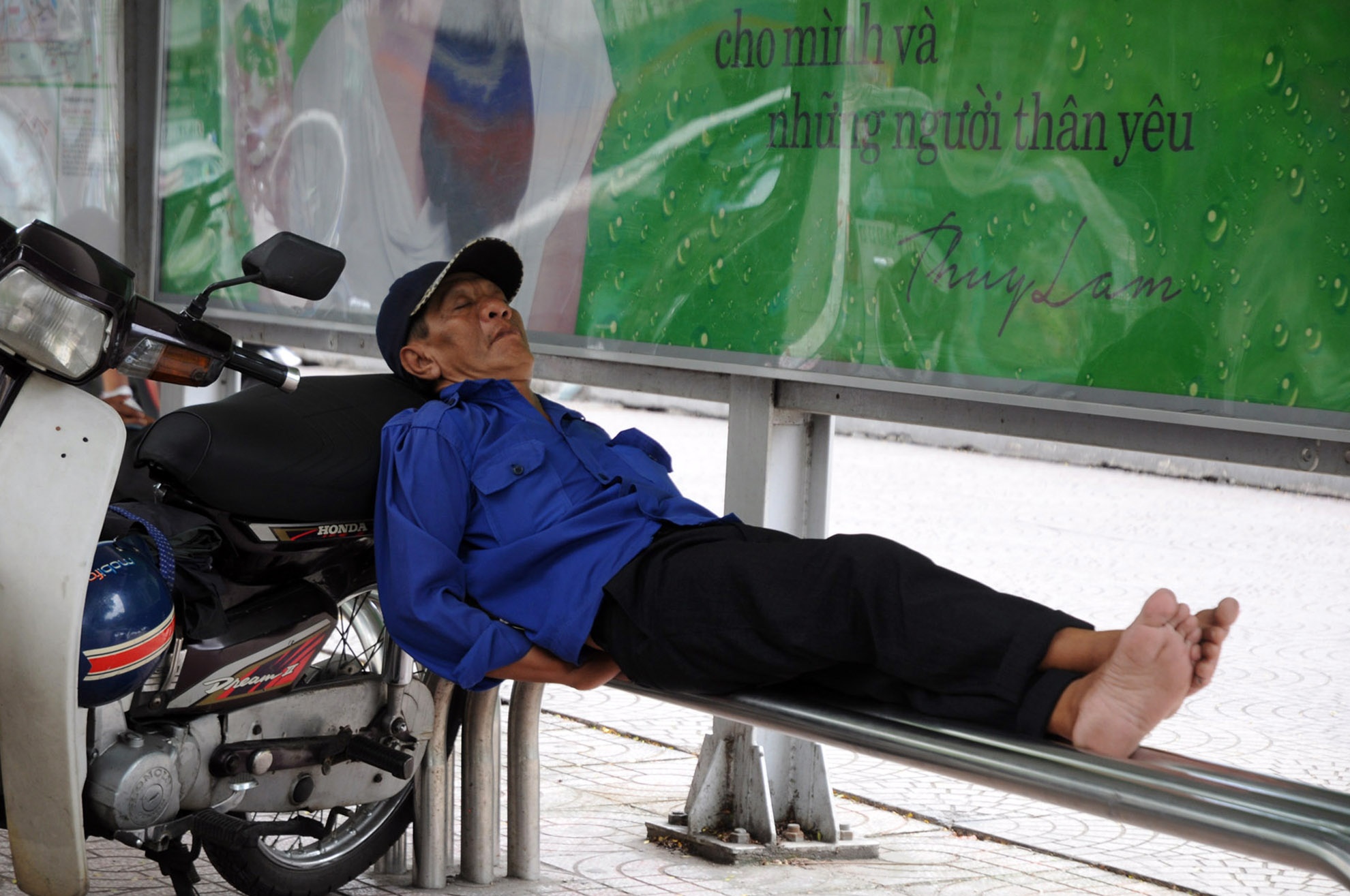Bác xe ôm ngã lưng ngay trên nhà chờ xe bus, nơi “giấc ngủ tốt cho mình và người thân”.
