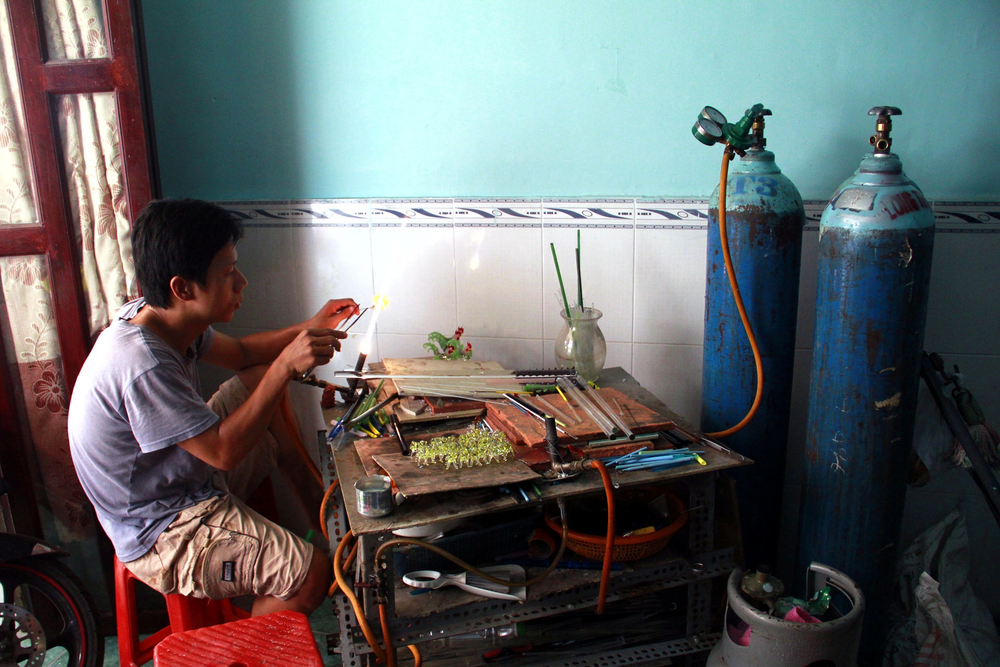 Nơi làm việc của anh chỉ đơn giản là một góc nhỏ vọn vẹn vài mét vuông với vô số những thanh thủy tinh đủ màu,  đủ kích thước các loại. và dụng cụ của anh cũng chỉ đơn giản là một ngọn đèn với nhiệt độ cực cao trên 1000 độ C mà thôi. “Công cụ” quan trọng nhất chính là bàn tay tài hoa của anh.