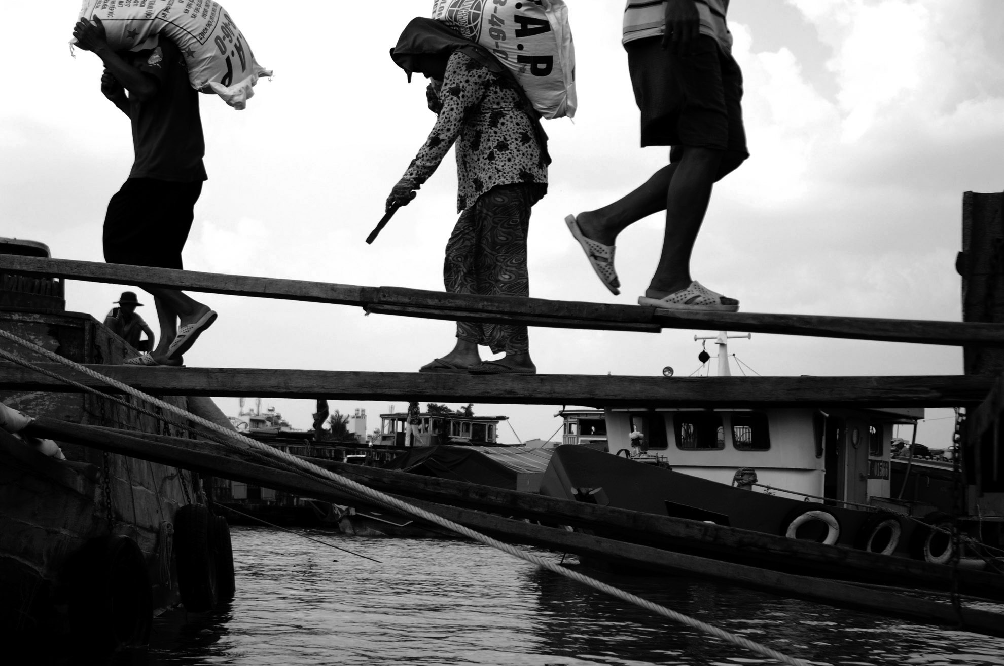 Quảng đường cõng những bao phân từ xe tải lên thuyền khá ngắn, nhưng lại ẩn chứa nhiều hiểm nguy vì phải đi qua những tấm ván nhỏ hẹp chỉ vừa đủ bàn chân.