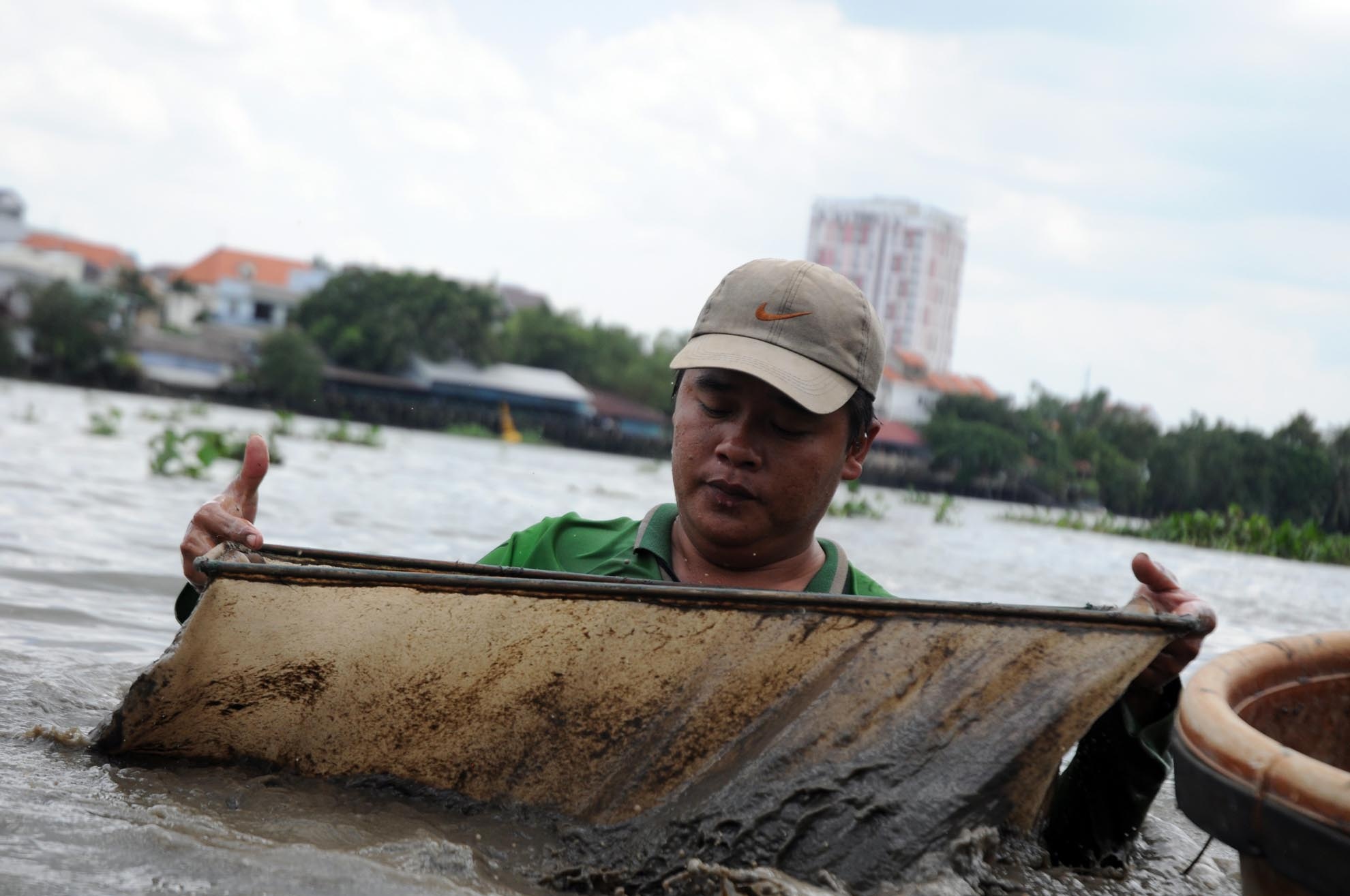 Sau khi xác định được địa điểm có nhiều trùn chỉ, anh Vinh ngụp lặn xuống đáy sông để vớt trùn chỉ lẫn với bùn đất bằng chiếc vợt đan bằng lưới. 