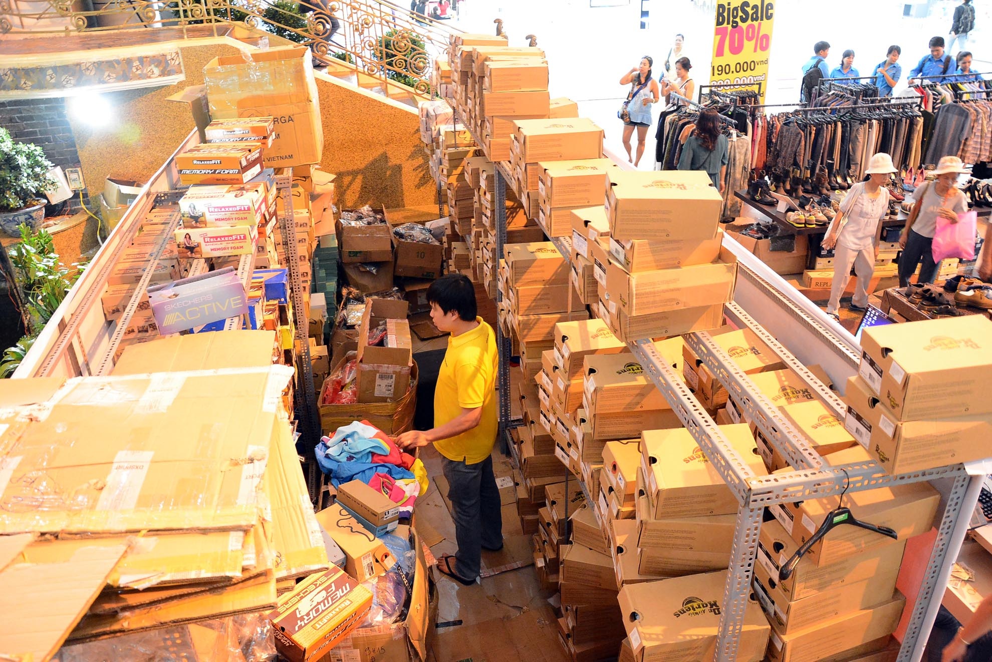 Nhân viên của gian hàng thời trang đang gom quần áo, giày dép vào thùng để chuẩn bị chuyển đi trong khi bên cạnh là một gian hàng đang cố bán vét hàng hoá nhằm thu lại chút vốn liếng đã bỏ ra.