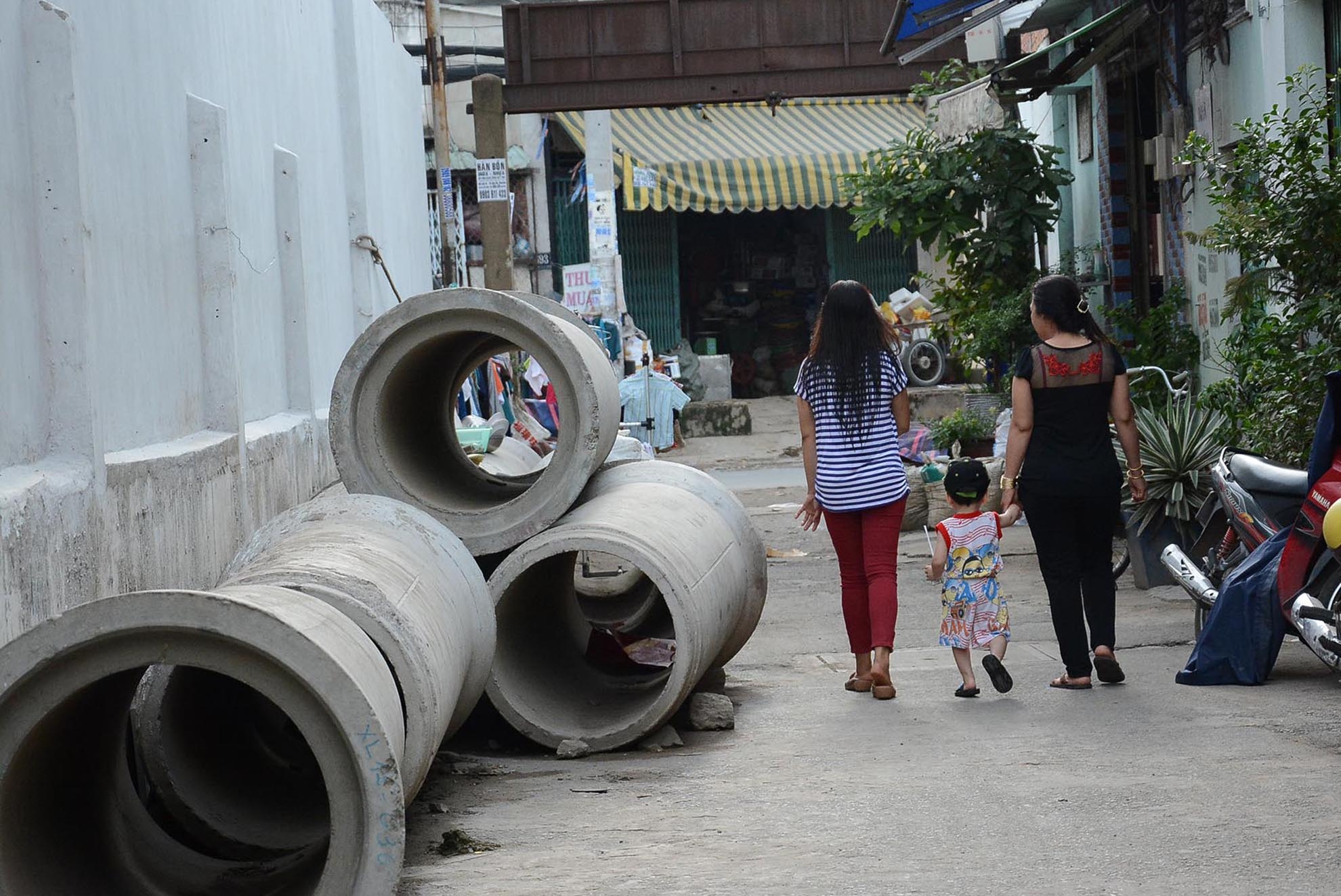 Những ống cống nằm dọc trong con hẻm 958 An Dương Vương không được che chắn nên rất nguy hiểm. Trong ảnh: Nhiều gia đình sợ ống cống lăn ra đường bất cứ lúc nào nên phải dắt con nhỏ đi qua đoạn hẻm này.