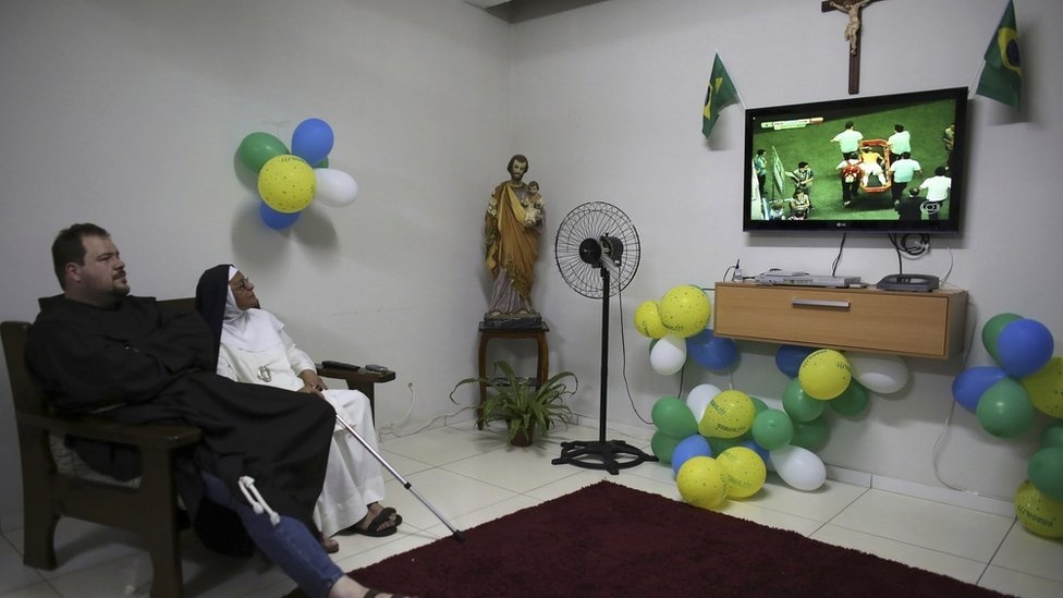 A priest from the Franciscan order and a nun from the enclosed monastery of Imaculada Conceicao watch on television as Brazil's Neymar grimaces as he is carried off the pitch after being injured in the 2014 World Cup quarter-final.