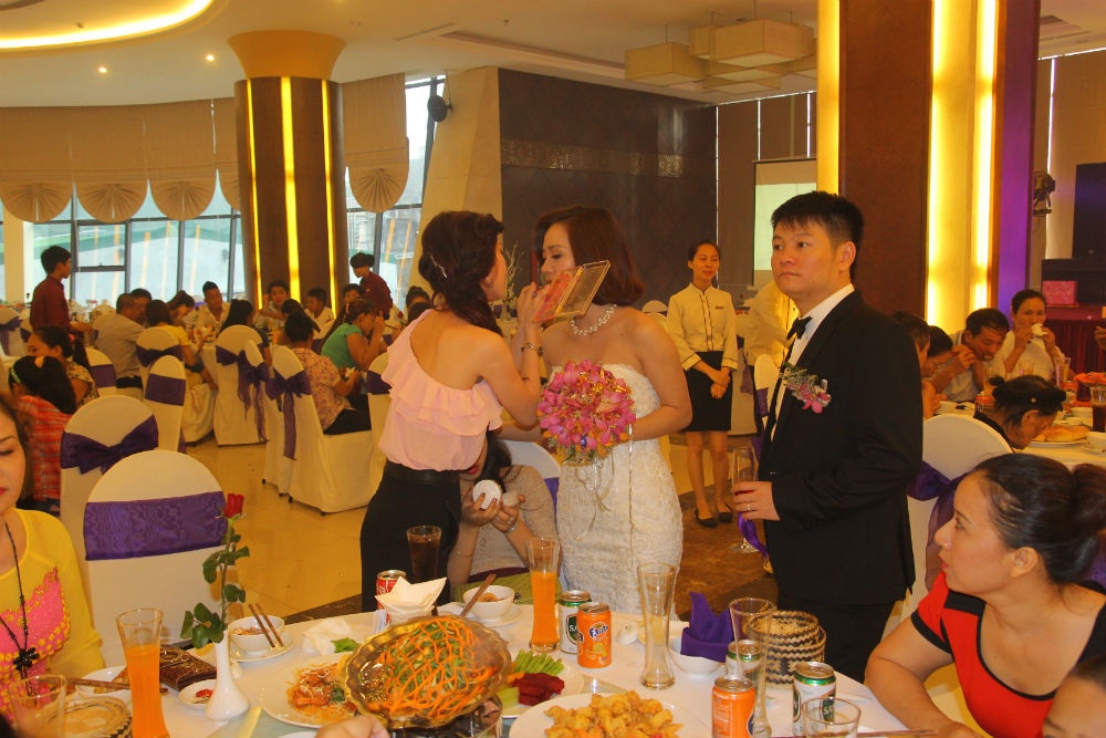 Cô dâu đang trang điểm trong lễ cưới, còn chú rể ngẩn ngơ đứng nhìn.