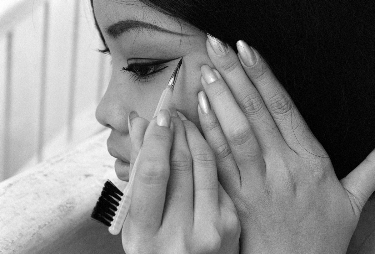 Một phụ nữ đang kẻ mắt bên bàn trang điểm.