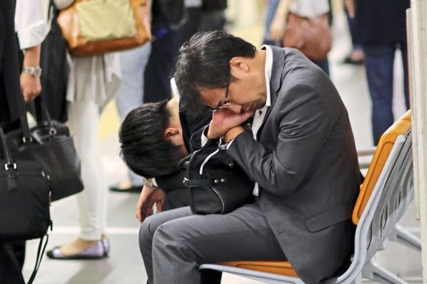 Người đàn ông ngủ gật trên ghế ngồi ở trạm tàu điện ngầm tại Tokyo sau giờ làm. Ảnh: AFP