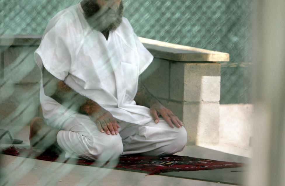 Một tù nhân quỳ và cầu nguyện Trại 4. Khan cho biết điều tra viên thường bắt tù nhân trút hết quần áo, rồi trói họ vào các cây cột. Tù nhân còn liên tục bị nhấn đầu vào nước đá.