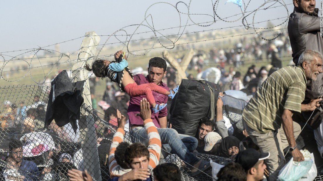 Một người đàn ông giúp bé gái vượt qua hàng rào biên giới ở Thổ Nhĩ Kỳ bị phá vỡ trước dòng người tị nạn. Ảnh: AFP