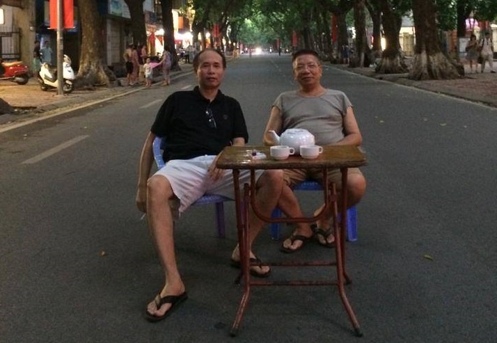 Hai nguoi dan ong ngoi giua duong pho Ha Noi uong tra hinh anh