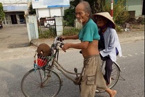 Cụ ông dắt xe đạp chở cụ bà đi bán mít