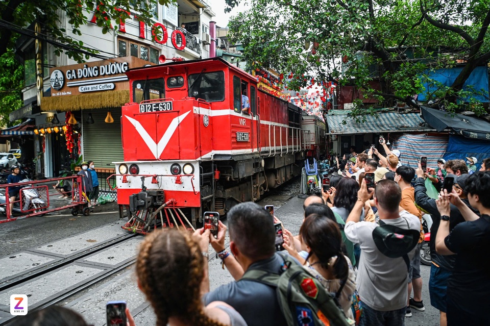 Du khách ghi lại cảnh đoàn tàu chạy qua phố cà phê đường tàu từ phía ngoài rào chắn, sáng 2/7. Ảnh: Châu Sa.